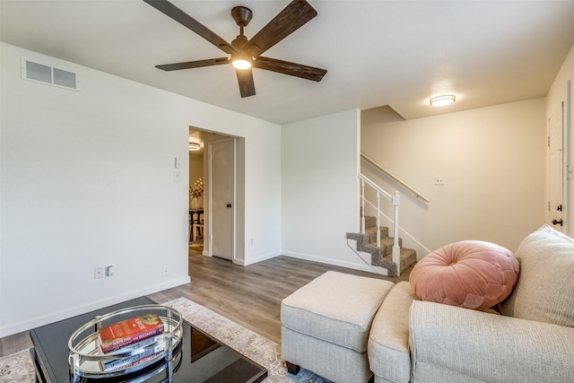 living room with wood finished floors, visible vents, baseboards, ceiling fan, and stairs