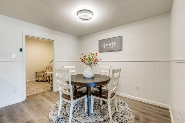 dining space with a textured ceiling, wood finished floors, and wainscoting