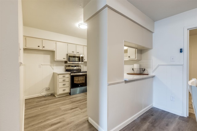 kitchen featuring stainless steel appliances, decorative backsplash, light countertops, and light wood finished floors