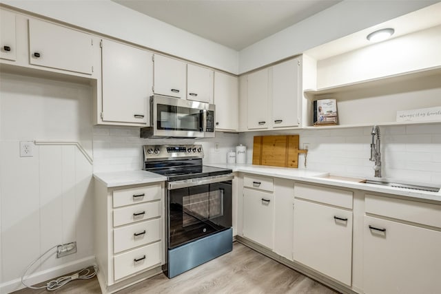 kitchen with open shelves, a sink, light countertops, appliances with stainless steel finishes, and light wood-type flooring