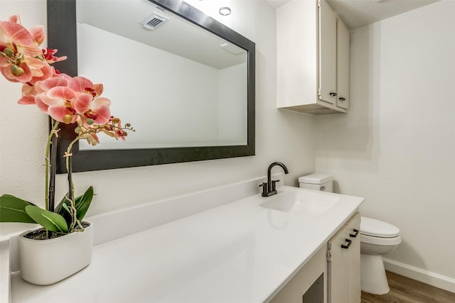 bathroom with visible vents, toilet, wood finished floors, baseboards, and vanity