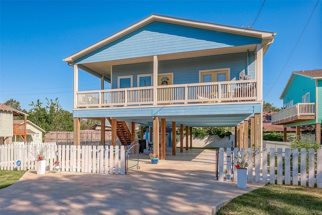 coastal home featuring fence, stairway, covered porch, a carport, and driveway