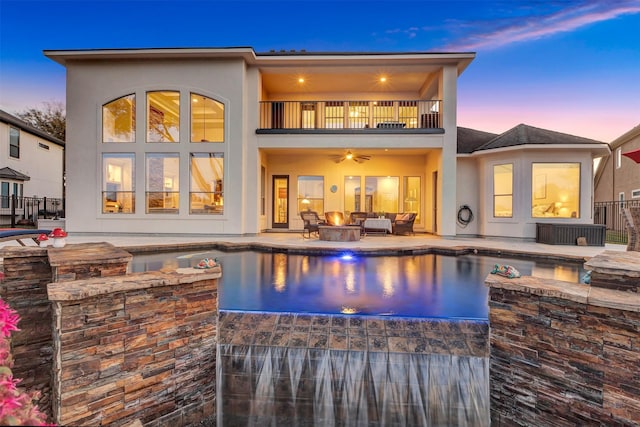 back of property at dusk featuring a balcony, an outdoor pool, stucco siding, a patio area, and an outdoor hangout area