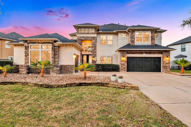 prairie-style home with a front yard, an attached garage, stucco siding, concrete driveway, and stone siding