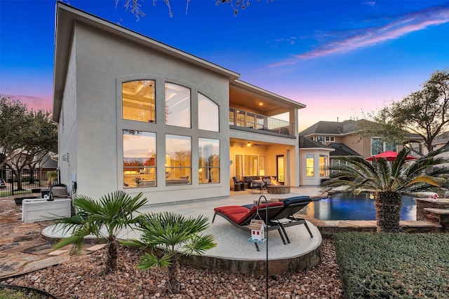 rear view of house with fence, stucco siding, a balcony, a ceiling fan, and a patio