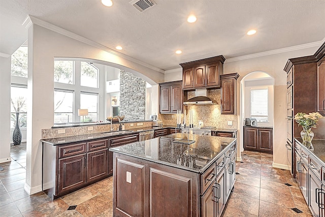 kitchen featuring visible vents, a sink, under cabinet range hood, backsplash, and a center island