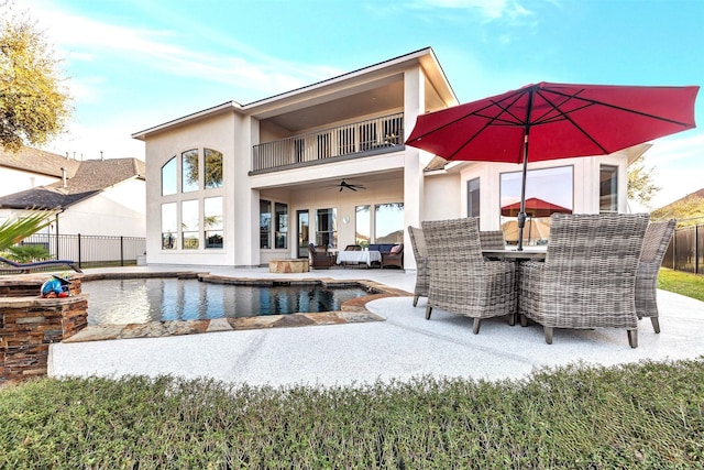 rear view of property featuring a balcony, outdoor dining area, fence, and stucco siding