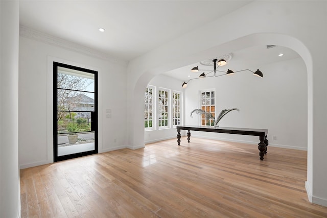 foyer entrance featuring arched walkways, a healthy amount of sunlight, baseboards, and light wood-style floors