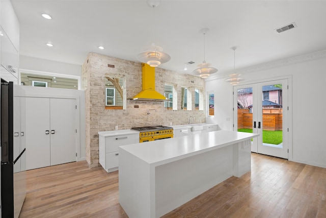 kitchen with double oven range, visible vents, light countertops, white cabinetry, and wall chimney exhaust hood