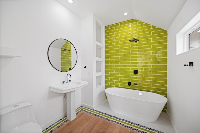 bathroom with wood finished floors, lofted ceiling, recessed lighting, a freestanding bath, and toilet