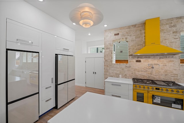 kitchen with white cabinetry, light countertops, freestanding refrigerator, exhaust hood, and modern cabinets