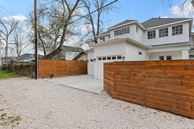 view of front of home with a fenced front yard, concrete driveway, and roof with shingles