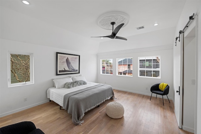 bedroom with visible vents, baseboards, lofted ceiling, a barn door, and light wood-style flooring