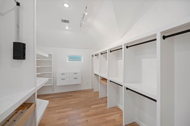 walk in closet with a barn door, visible vents, light wood-type flooring, and vaulted ceiling