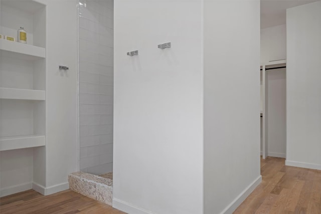 bathroom featuring built in shelves, baseboards, wood finished floors, and a tile shower