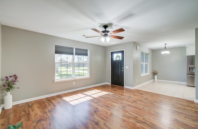 foyer entrance featuring ceiling fan with notable chandelier, baseboards, and light wood-type flooring