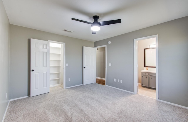 unfurnished bedroom featuring visible vents, baseboards, light colored carpet, and a walk in closet