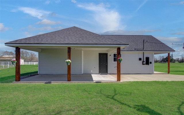 rear view of house featuring a patio, a lawn, and roof with shingles