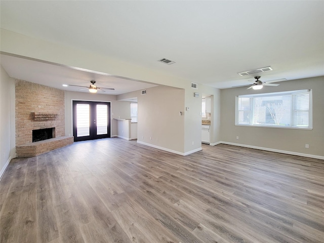 unfurnished living room with visible vents, a brick fireplace, baseboards, and wood finished floors