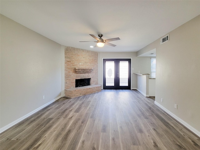 unfurnished living room with visible vents, a brick fireplace, baseboards, french doors, and wood finished floors