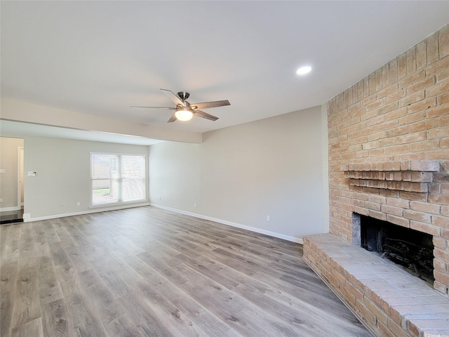 unfurnished living room featuring a brick fireplace, wood finished floors, baseboards, and ceiling fan