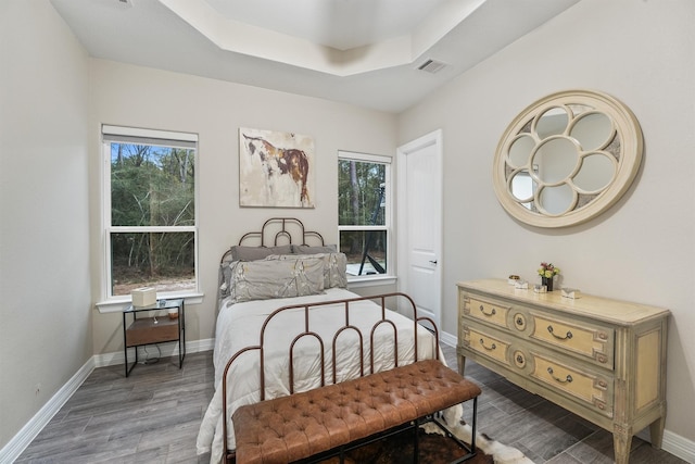 bedroom with a tray ceiling, wood finished floors, visible vents, and baseboards