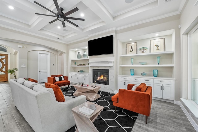 living area featuring built in features, a premium fireplace, arched walkways, coffered ceiling, and a ceiling fan