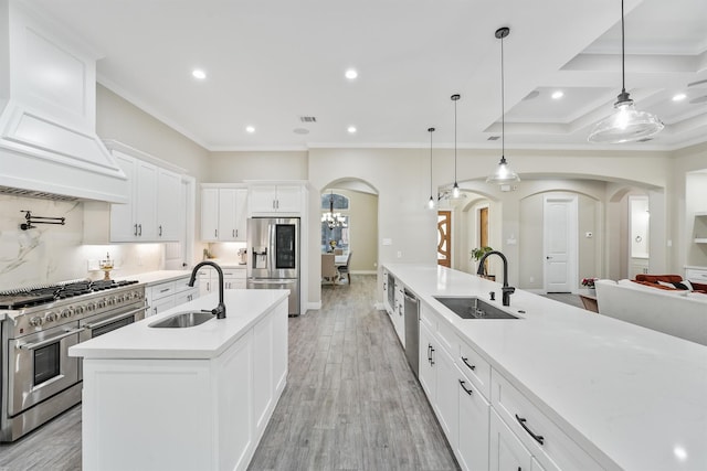 kitchen with premium range hood, arched walkways, appliances with stainless steel finishes, and a sink