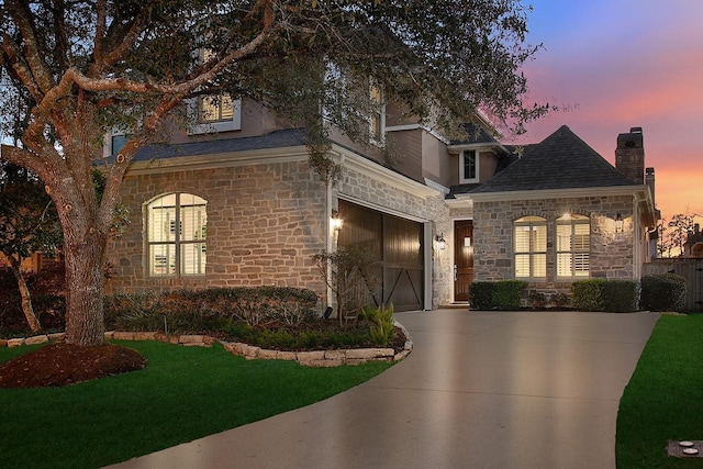 french provincial home featuring an attached garage, a shingled roof, a yard, stone siding, and driveway