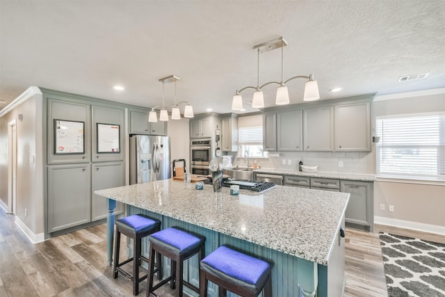 kitchen with visible vents, a breakfast bar, gray cabinets, appliances with stainless steel finishes, and light wood finished floors