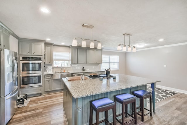 kitchen with gray cabinets, stainless steel appliances, ornamental molding, and a sink