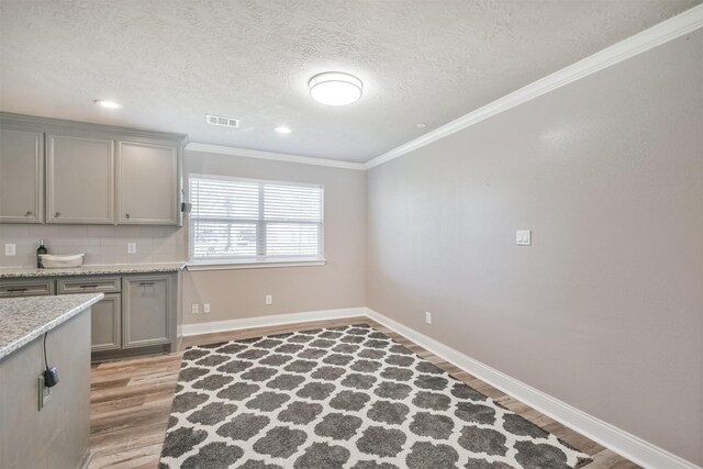 kitchen with light wood-type flooring, visible vents, gray cabinetry, backsplash, and crown molding