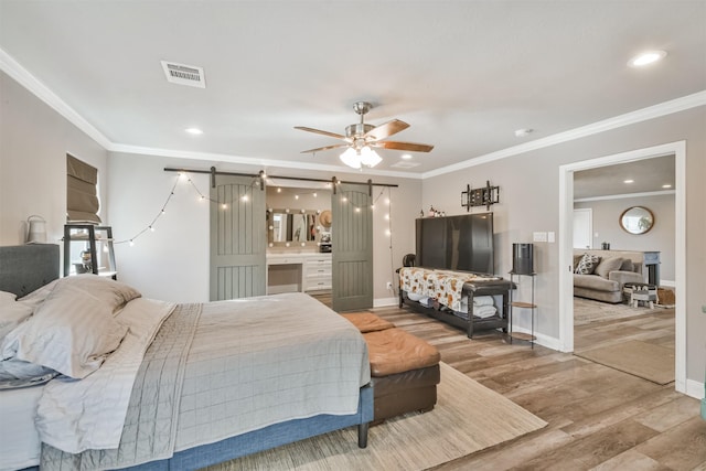 bedroom featuring a barn door, light wood-style floors, and crown molding