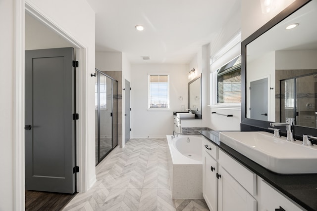 full bath featuring a tub with jets, visible vents, two vanities, a sink, and a shower stall