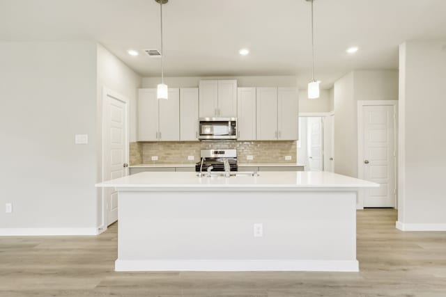 kitchen featuring light wood-type flooring, stainless steel appliances, decorative backsplash, and light countertops