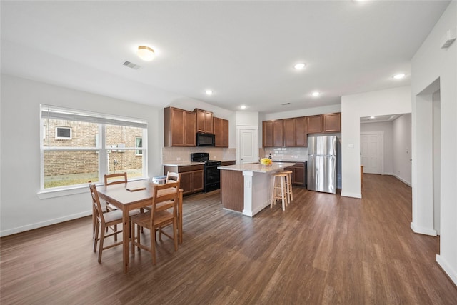 kitchen featuring a breakfast bar, dark wood-style flooring, black appliances, tasteful backsplash, and a center island