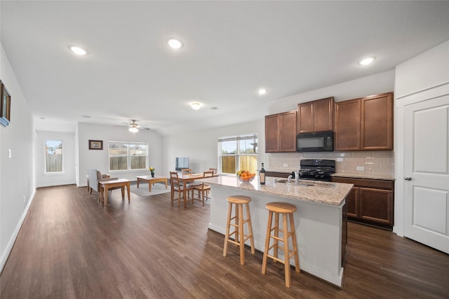 kitchen with black appliances, a sink, backsplash, dark wood finished floors, and a breakfast bar area