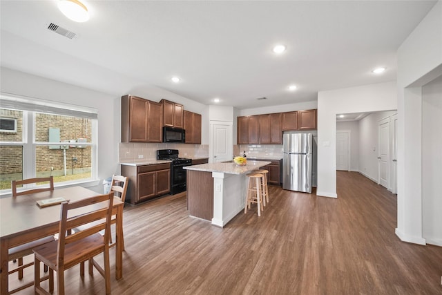 kitchen with visible vents, a kitchen bar, dark wood-type flooring, black appliances, and decorative backsplash