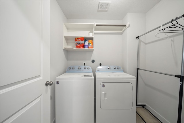 clothes washing area with laundry area, washing machine and dryer, visible vents, and a textured ceiling