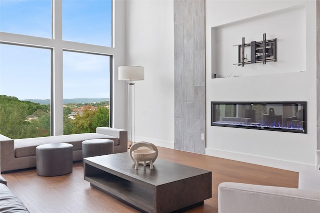 living area with a glass covered fireplace, baseboards, a towering ceiling, and wood finished floors