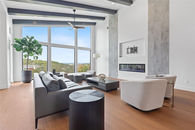 living area with a glass covered fireplace, beamed ceiling, baseboards, and wood finished floors