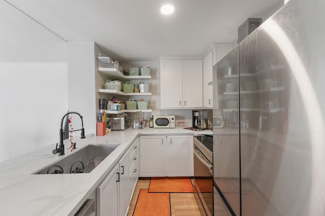 kitchen featuring light stone countertops, open shelves, a sink, stainless steel appliances, and white cabinets