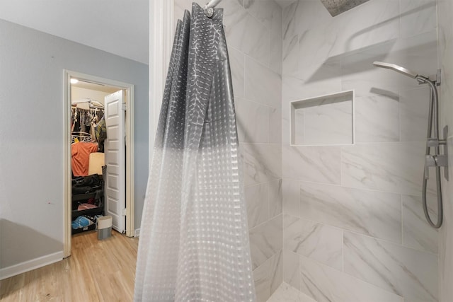 full bath featuring a spacious closet, wood finished floors, baseboards, and tiled shower