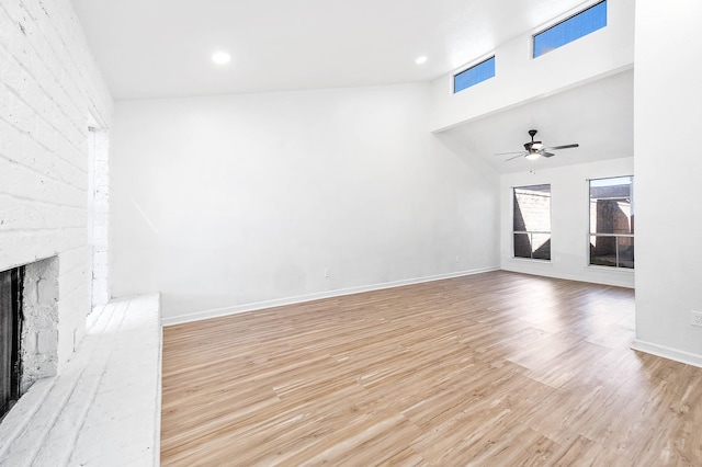 unfurnished living room featuring a high ceiling, a brick fireplace, a ceiling fan, baseboards, and wood finished floors