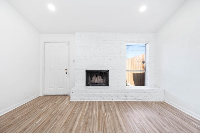 unfurnished living room with baseboards, wood finished floors, and a brick fireplace