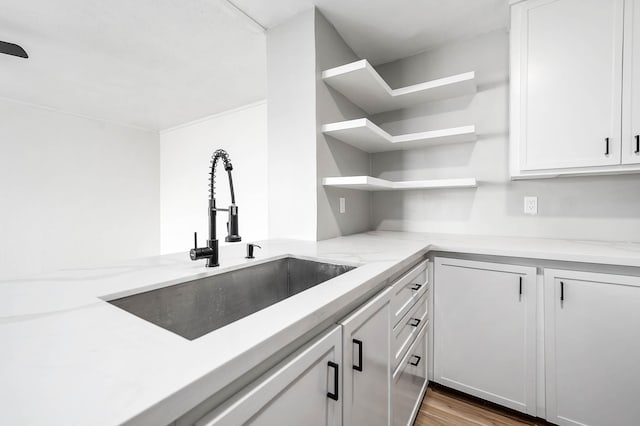 kitchen with light stone counters, white cabinetry, open shelves, and a sink