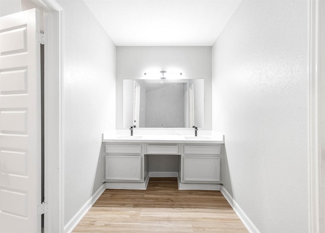 bathroom featuring double vanity, a sink, wood finished floors, and baseboards