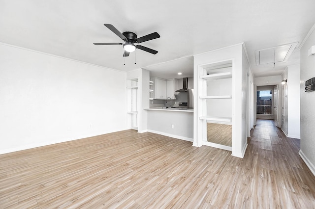 unfurnished living room featuring attic access, light wood finished floors, a sink, a ceiling fan, and baseboards