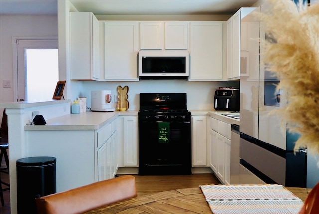 kitchen with a peninsula, white cabinets, light countertops, white microwave, and black range with gas cooktop