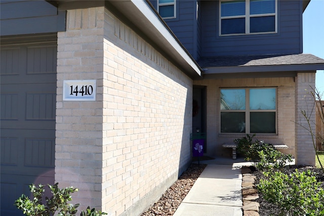 view of exterior entry with brick siding and roof with shingles